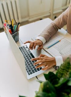 A business professional typing on a laptop at a well-organized office desk with plants and stationery.